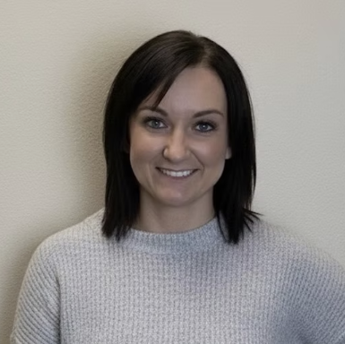 Woman with shoulder-length dark hair wearing a light gray sweater against a plain background
