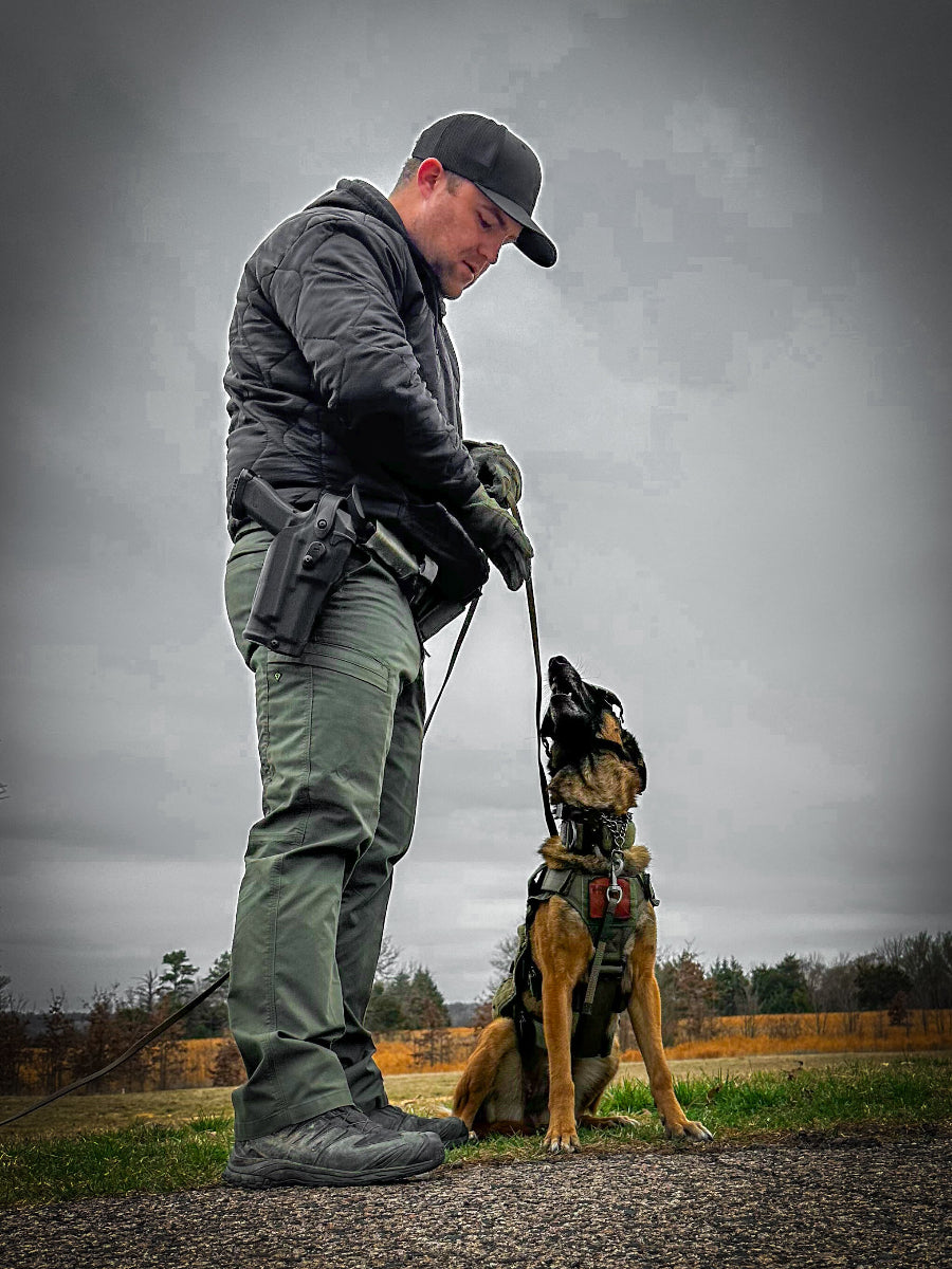 Man in tactical gear with a dog on a leash against a gray sky